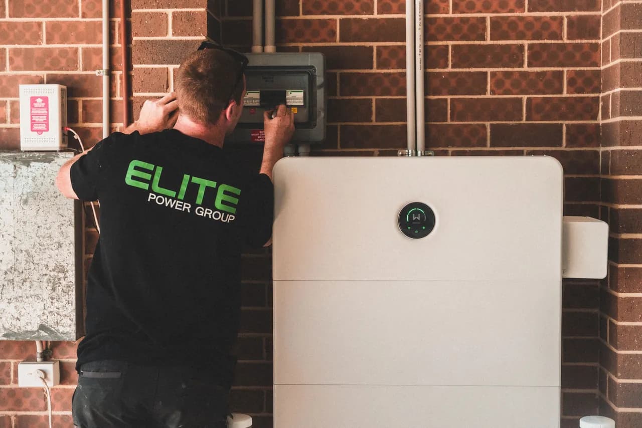 An electrician connecting the cabling of a wall-mounted battery energy-storage unit during installation.