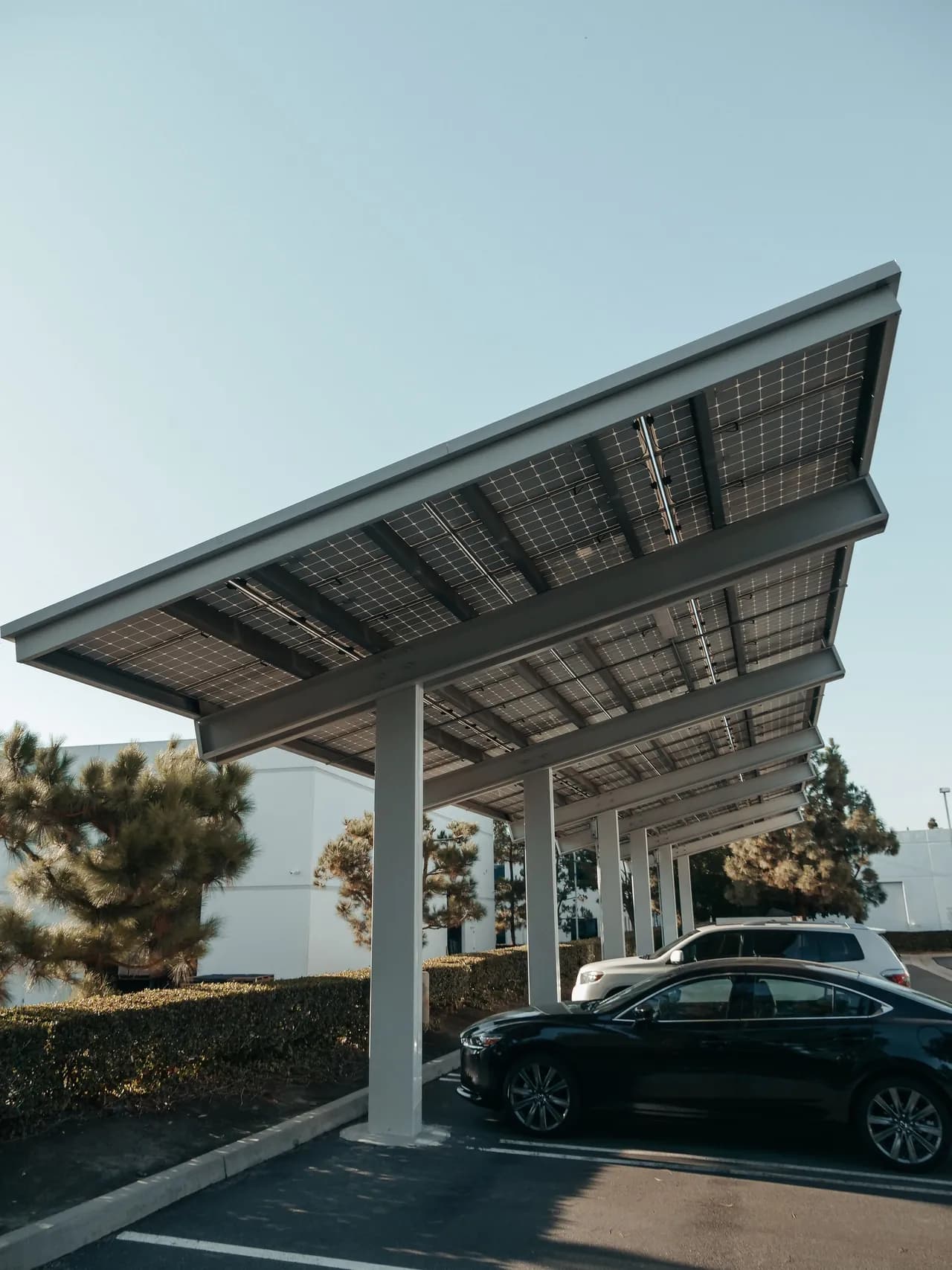 Cars parked in the shade of a solar carport, with photovoltaic panels forming the canopy roof above the parking bays.