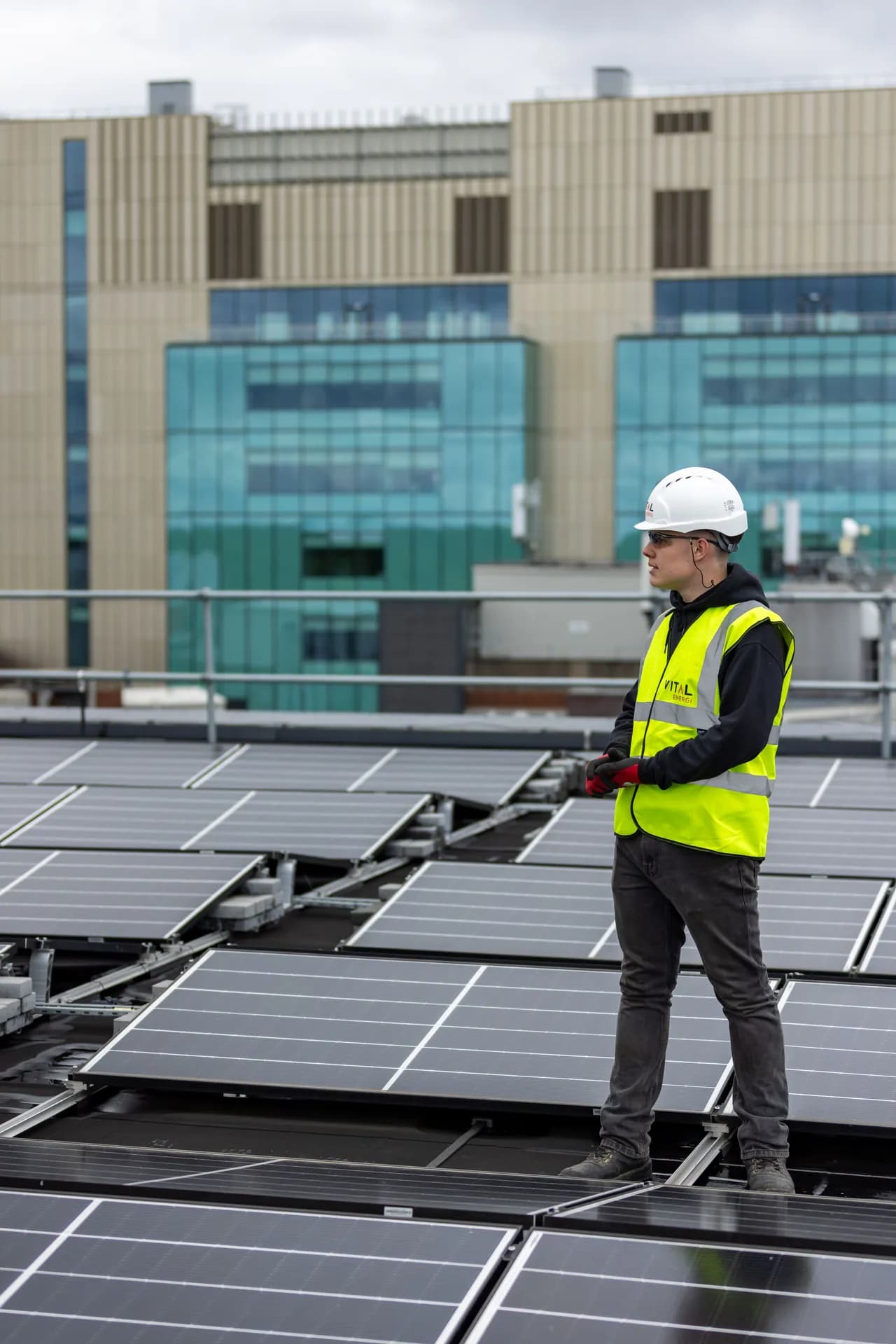 A worker in a high-visibility vest and helmet standing between rows of rooftop solar panels, checking the array.