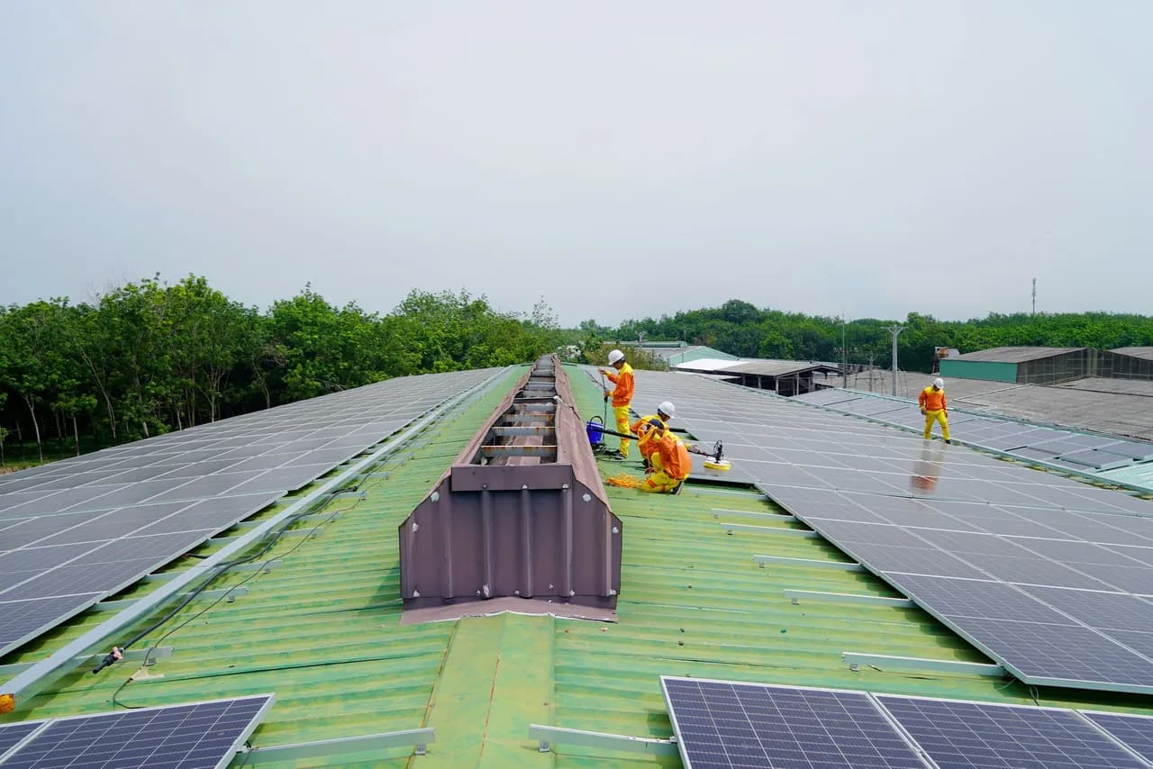 An installation crew in hard hats lifting solar panels into position on a large flat rooftop.