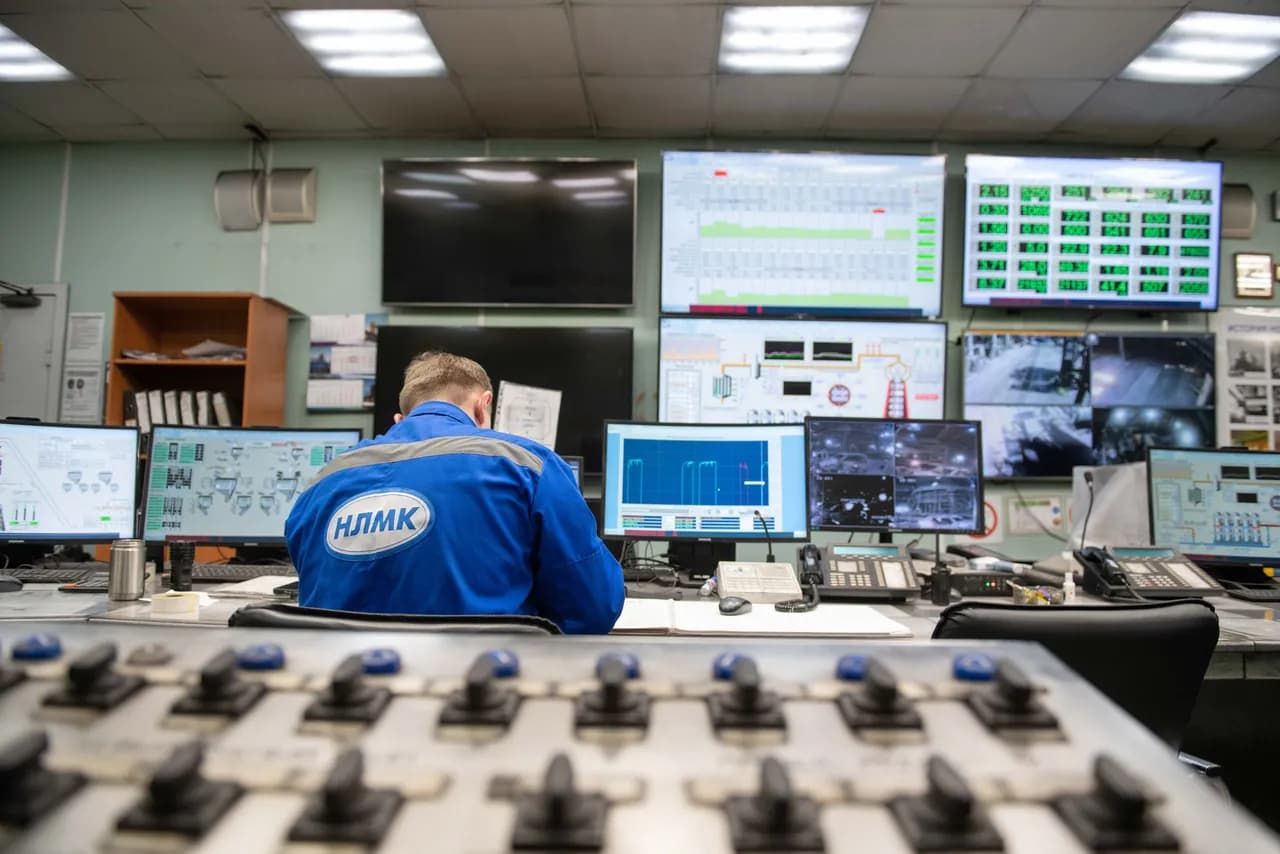 An engineer at a control-room workstation watching a bank of screens that display live plant data.