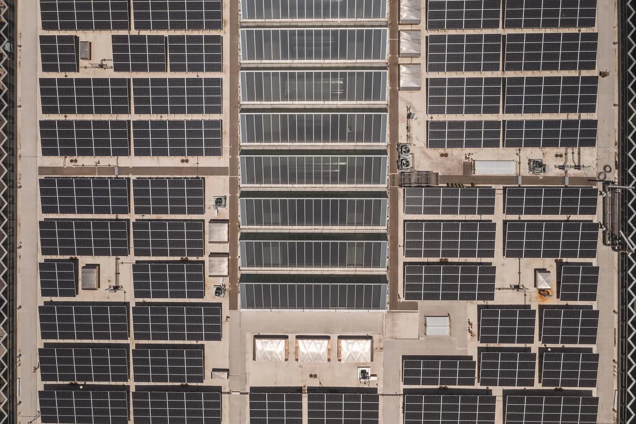 Drone view looking down on a large industrial rooftop covered by a neat grid of solar panels.