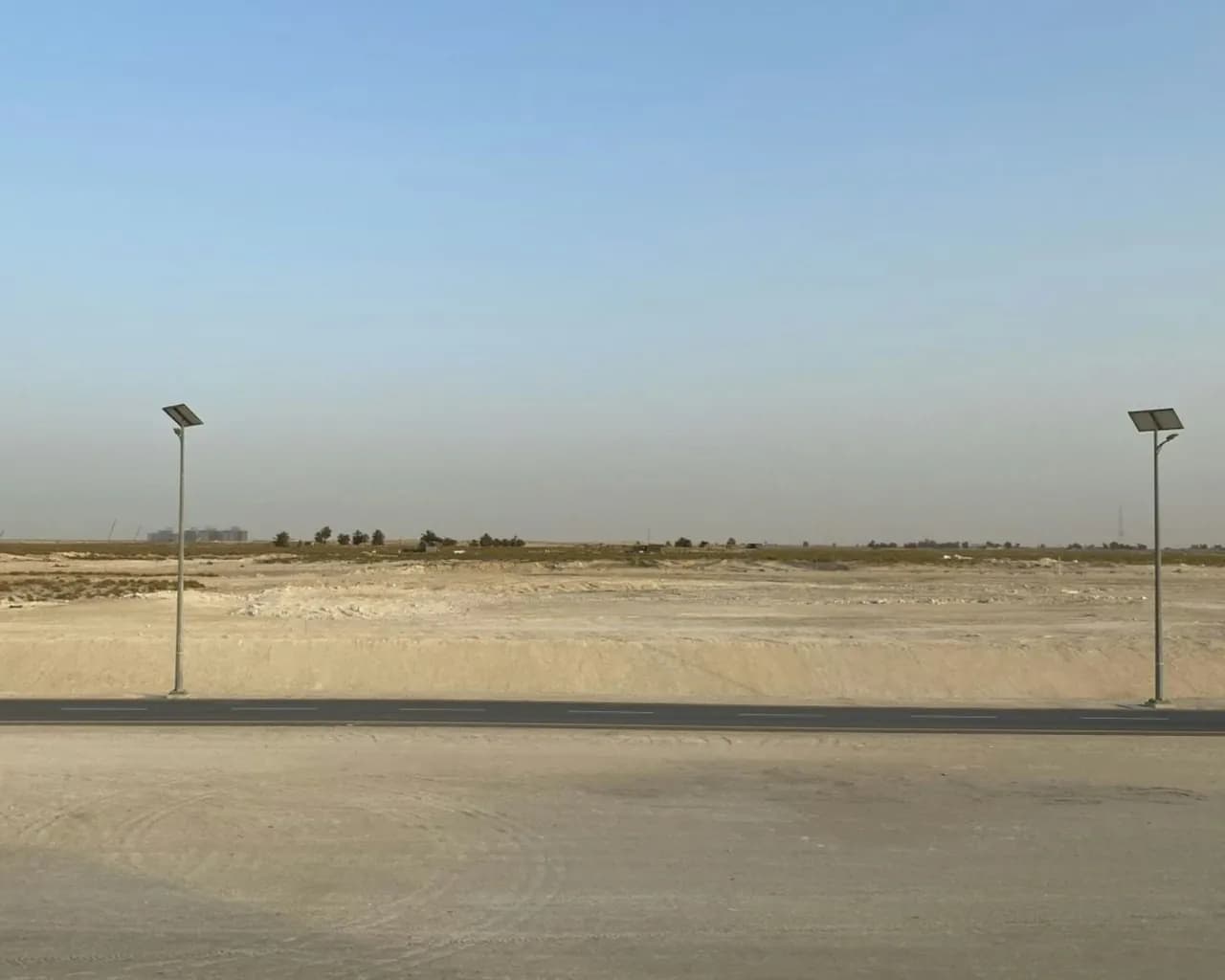 Two solar-powered street lights standing on either side of an empty asphalt road crossing bare desert sand.
